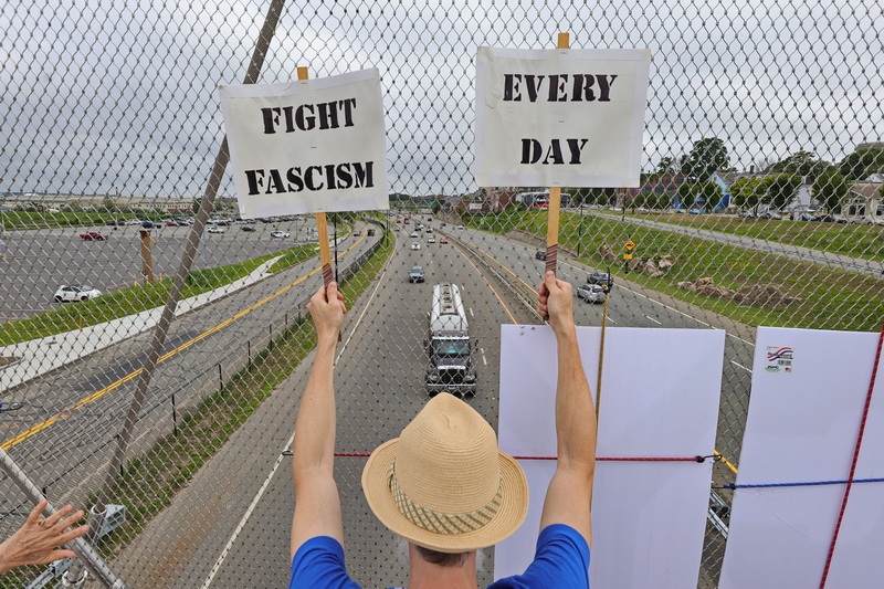 Jonathan Danforth and fellow Good Trouble protestors hold up signs to passing cars from the pedestrian bridge crossing Route 18 in New Bedford, MA. PHOTO PETER PEREIRA