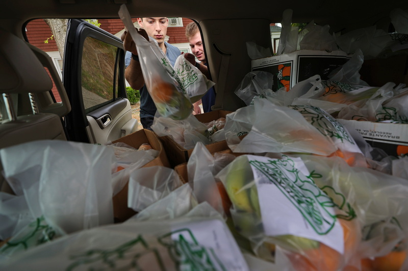 Grayson Cohen and Marc London grab bags filled with fruit from their SUV, before distributing them to residents of the Blue Meadows housing complex on Dartmouth Street in New Bedford. Tabor Academy senior Marc London started Marc's Market last summer to provide fruit to residents of government subsidized housing complexes in New Bedford, MA.  PHOTO PETER PEREIRA