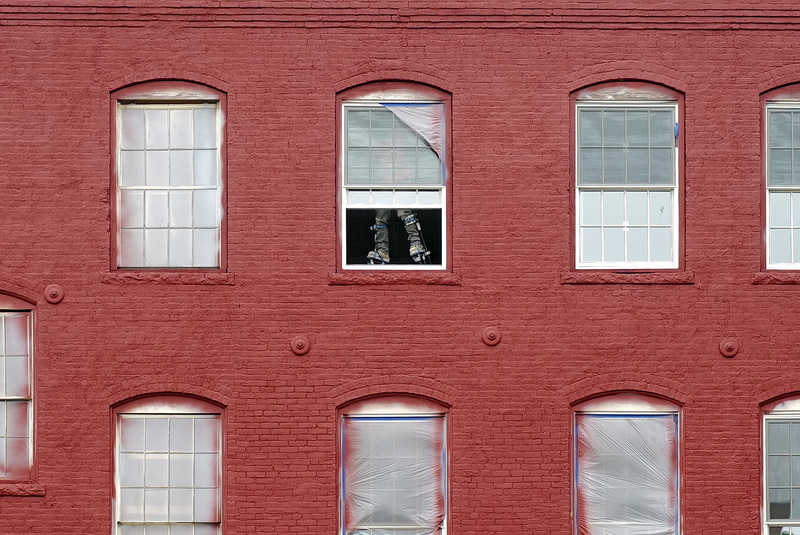 The legs of a painter on stilts can be seen through the partially opened window on the top floor of the former mill at the bottom of Elm Street in New Bedford, MA being converted into apartments. PHOTO PETER PEREIRA