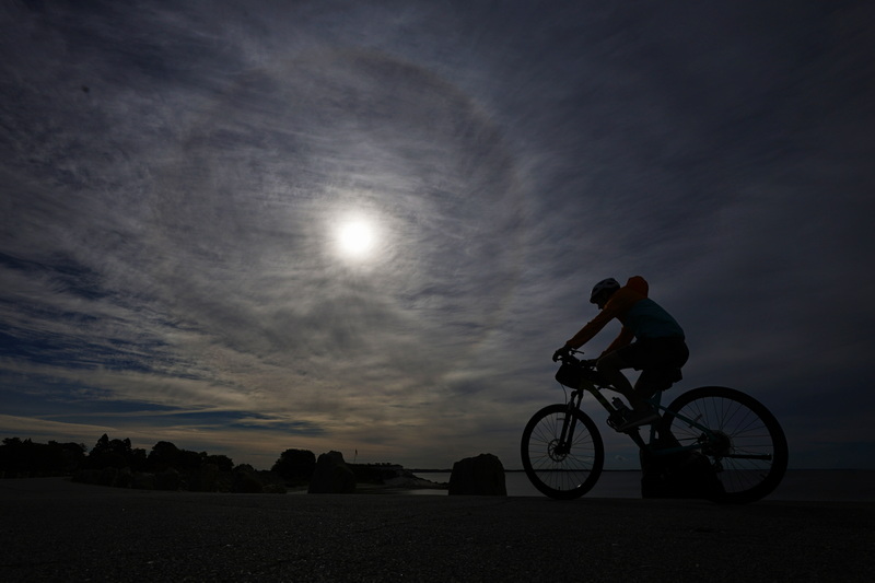 A cyclist pedals his bicycle along the hurricane barrier at Fort Phoenix in Fairhaven, MA with a rare sun halo visible in the sky above. PHOTO PETER PEREIRA