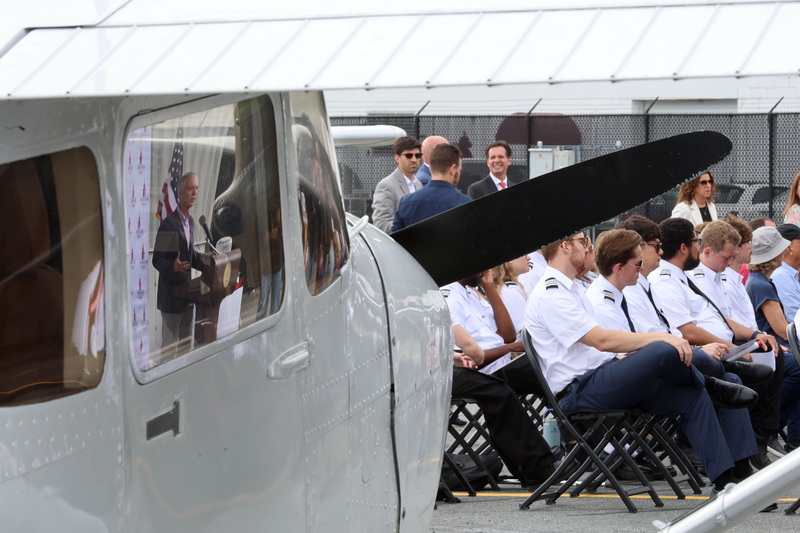 Mayor Jon Mitchell is reflected on the window of a training aircraft as students and instructors listen to him speak at a ceremony marking the official opening of a new Bridgewater State University aviation hangar at New Bedford airport. PHOTO PETER PEREIRA