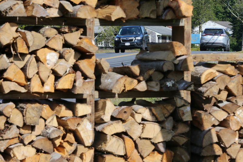 Vehicles drive along Main Road as seen through gaps in firewood reams for sale on Kirby Road in Westport, MA. PHOTO PETER PEREIRA