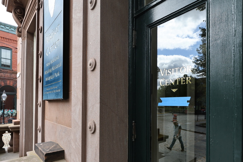 A man is reflected on the window door to the entrance of the New Bedford Whaling National Historic Park Visitor Center in New Bedford, as he crosses William Street in downtown New Bedford.  The tape hides hours of operation due to the center has been closed due to govermental shut down. PHOTO PETER PEREIRA