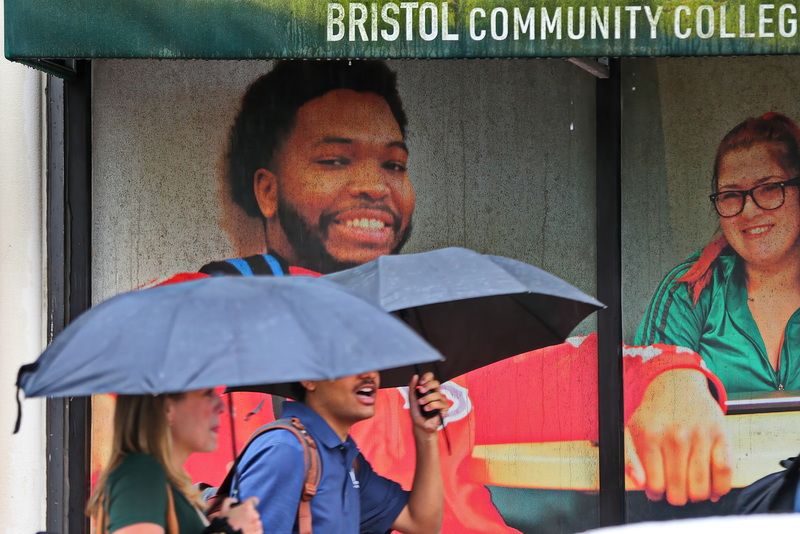 The students in the pictures on the windows of Bristol Community College's downtown New Bedford campus are smiling as they watch other students seeking refuge from the heavy rain outside. PHOTO PETER PEREIRA