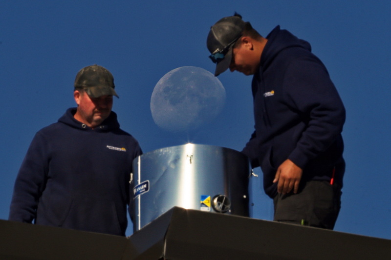 The moon seemingly emerges from the air duct two AirMasters technicians are installing on the roof of the YMCA in downtown New Bedford, MA. PHOTO PETER PEREIRA
