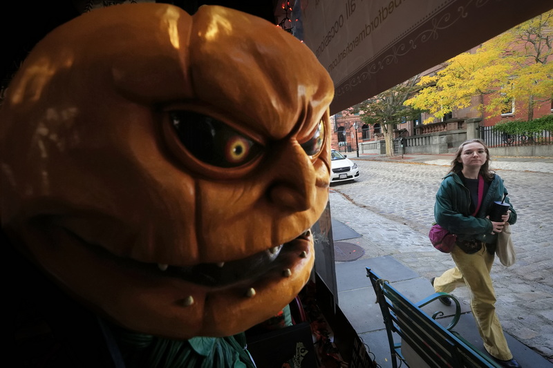 A woman walking down William Street finds herself under the watchful eye of 'Jack' the pumpkin goblin inside of The Bedford Merchant in downtown New Bedford, MA.  PHOTO PETER PEREIRA