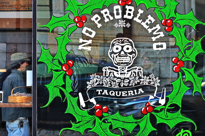 Elysa Pereira, right, is seen through the festive No Problemo window decoration as she takes a patron's order at the downtown New Bedford, MA taqueria. PHOTO PETER PEREIRA