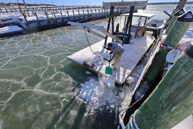 Bob Veeder of Triad Boatworks shovels the accumulated snow from the company mooring barge onto a frozen Mattapoisett harbor on a cold morning. PHOTO PETER PEREIRA