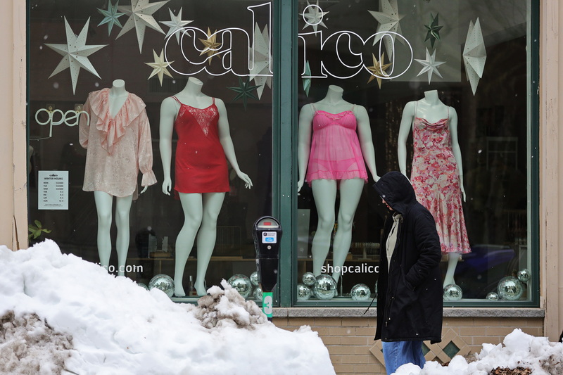 Snow starts to fall as a woman walks past the storefront of Calico on Union Street in New Bedford, MA displaying spring women's wear on a cold day. PHOTO PETER PEREIRA