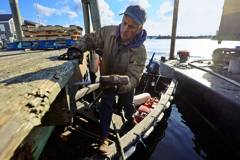 Wayne Manchester stands on a small boat as he hammers a bolt into the new wood sections he has replaced on the dock he is fixing in Westport, MA. PHOTO PETER PEREIRA