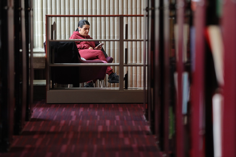 A woman is framed by an empty book case as she reads on her smartphone at the UMass Dartmouth library. PHOTO PETER PEREIRA