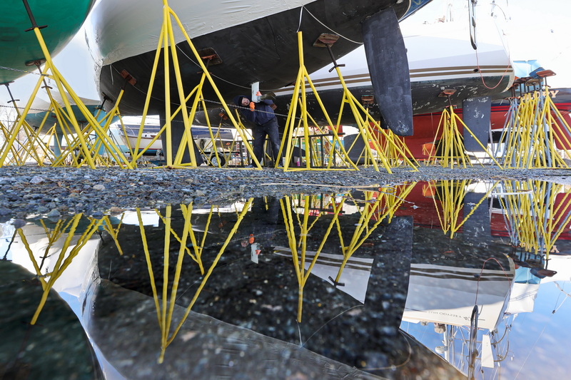 David Bergassi is reflected in a puddle as he makes repairs to the sail drive on a yacht at Barden's Boat Yard in Marion, MA.  PHOTO PETER PEREIRA
