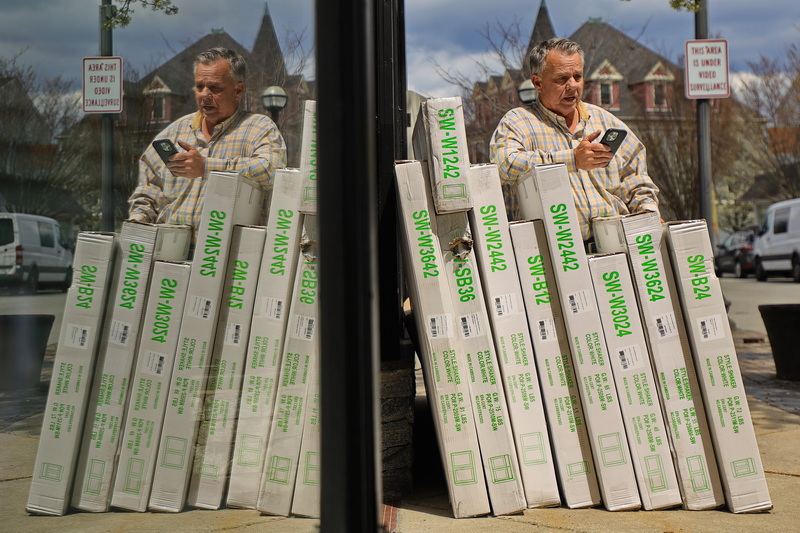 Joe Pereira, owner of Precision Window & Kitchen, is reflected on the windows of his store on Acushnet Avenue in New Bedford, MA as he stands next to a customer's order he is speaking with on the phone. PHOTO PETER PEREIRA