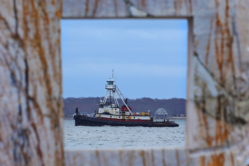 The tugboat Realist sails back into New Bedford harbor as seen through the gap in a granite sculpture installed on East Beach in New Bedford, MA. PHOTO PETER PEREIRA