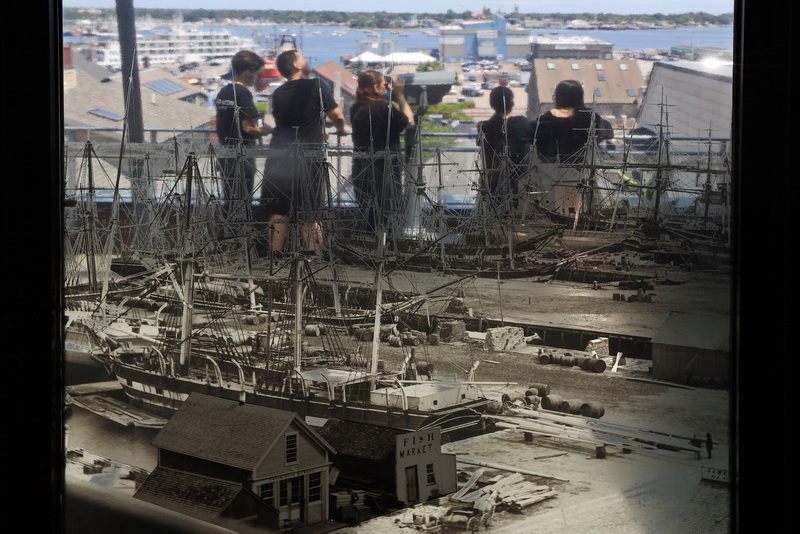 On July 8, 2026 visitors to the New Bedford Whaling Museum observe New Bedford's waterfront from the observation deck outside, as seen through a transparency on the window that depicts what the dock appeared like during the era of the city's whaling industry. PHOTO PETER PEREIRA