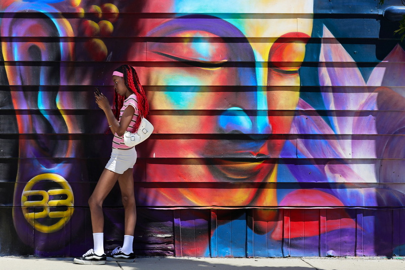 A young woman stands waiting for the bus on July 9, 2026, in front of a Buddha mural painted on the side of a building on Pleasant Street in New Bedford, MA. PHOTO PETER PEREIRA