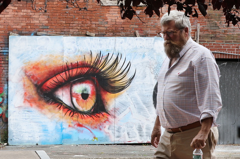 A painted eye looks on as a man crosses Wings Court in New Bedford, MA on July 22, 2026. PHOTO PETER PEREIRA