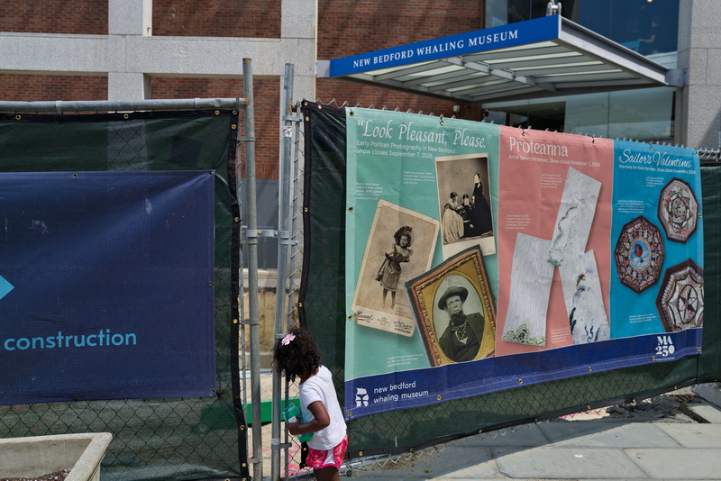 A young girl takes a peek through the retaining fence to see the construction underway at the entrance to the New Bedford Whaling Museum on August 12, 2026. PHOTO PETER PEREIRA