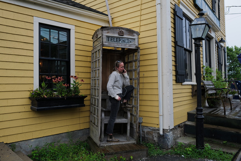 Lissa Pocze seeks refuge from the heavy rain by making a call on her smartphone inside the English telephone booth located outside Davoll's General Store in Dartmouth, MA, on September 1, 2026. PHOTO PETER PEREIRA