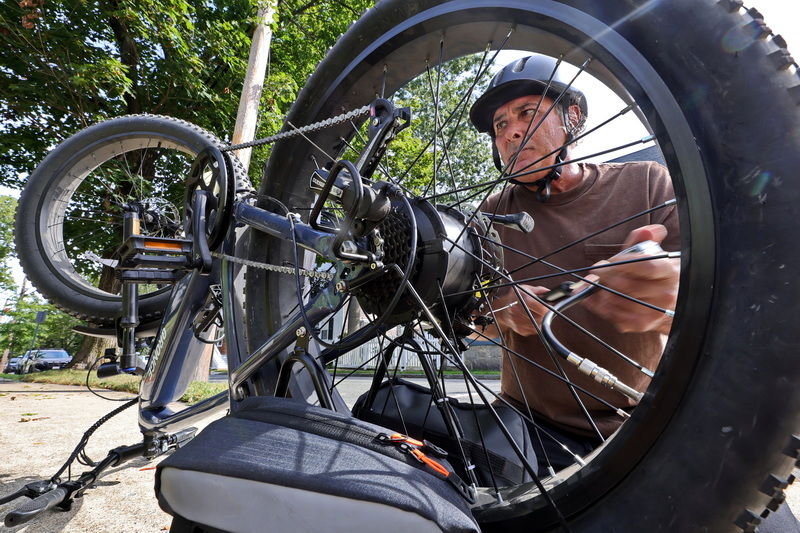 Brian finishes fixing a flat during his ride through Fairhaven, MA on September 2, 2026, keeping his eyes on the wheel as he works a hand pump to refill the rear tire on his e-bike. PHOTO PETER PEREIRA