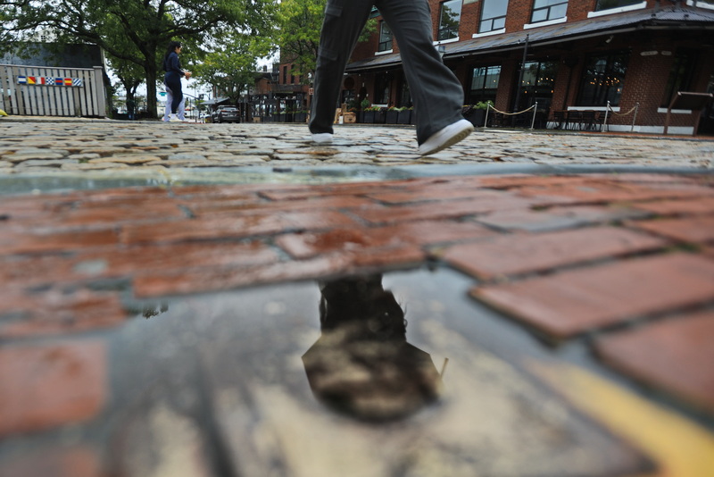 A woman walking up Union Street in New Bedford, MA on September 28, 2026 with umbrella in hand is reflected on a small puddle between bricks on the edge of the road, as rain continues to fall across the region. PHOTO PETER PEREIRA