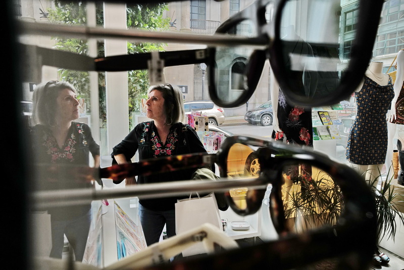 Maria DaSilva takes a look at the new and vintage clothing available at Calico on Union Street in New Bedford, MA on October 1, 2026 as seen through the sunglass rack. PHOTO PETER PEREIRA