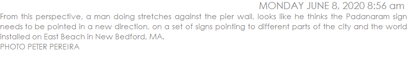 From this perspective, a man doing stretches against the pier wall, looks like he thinks the Padanaram sign needs to be pointed in a new direction, on a set of signs pointing to different parts of the city and the world installed on East Beach in New Bedford, MA.  