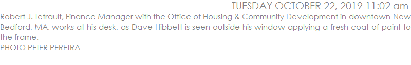 Robert J. Tetrault, Finance Manager with the Office of Housing & Community Development in downtown New Bedford, MA, works at his desk, as Dave Hibbett is seen outside his window applying a fresh coat of paint to the frame. 