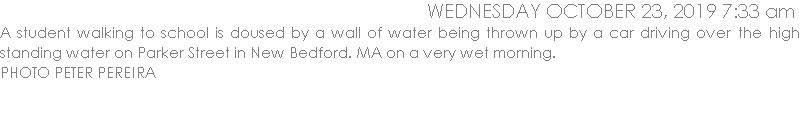A student walking to school is doused by a wall of water being thrown up by a car driving over the high standing water on Parker Street in New Bedford. MA on a very wet morning. 