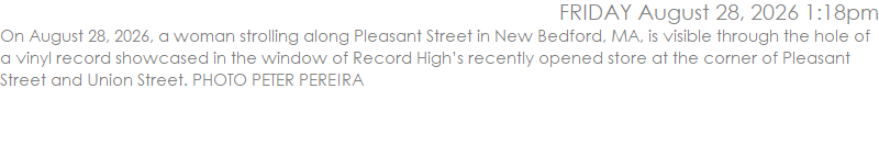 On August 28, 2026, a woman strolling along Pleasant Street in New Bedford, MA, is visible through the hole of a vinyl record showcased in the window of Record High�s recently opened store at the corner of Pleasant Street and Union Street. PHOTO PETER PEREIRA