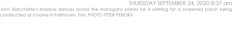 John Blanchette's shadow dances across the mahogany planks he is priming for a screened porch being constructed at a home in Fairhaven, MA. PHOTO PETER PEREIRA