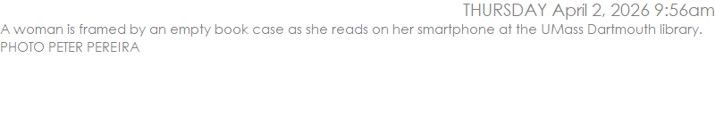 A woman is framed by an empty book case as she reads on her smartphone at the UMass Dartmouth library. PHOTO PETER PEREIRA