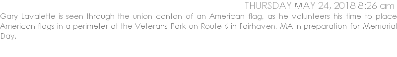 Gary Lavalette is seen through the union canton of an American flag as he volunteers his time to place American flags in a perimeter at the Veterans Park on Route 6 in Fairhaven in preparation for Memorial Day.