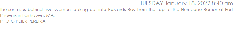 The sun rises behind two women looking out into Buzzards Bay from the top of the Hurricane Barrier at Fort Phoenix in Fairhaven, MA. 