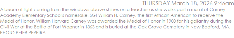 A beam of light coming from the windows above shines on a teacher as she walks past a mural of Carney Academy Elementary School's namesake, SGT William H. Carney, the first African American to receive the Medal of Honor. William Harvard Carney was awarded the Medal of Honor in 1900 for his gallantry during the Civil War at the Battle of Fort Wagner in 1863 and is buried at the Oak Grove Cemetery in New Bedford, MA. PHOTO PETER PEREIRA