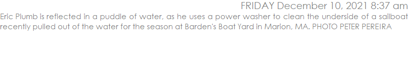 Eric Plumb is reflected in a puddle of water, as he uses a power washer to clean the underside of a sailboat recently pulled out of the water for the season at Barden's Boat Yard in Marion, MA. PHOTO PETER PEREIRA