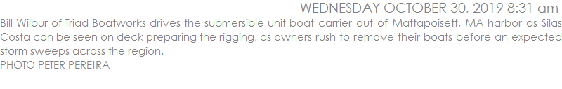 Bill Wilbur of Triad Boatworks drives the submersible unit boat carrier out of Mattapoisett, MA harbor as Silas Costa can be seen on deck preparing the rigging, as owners rush to remove their boats before an expected storm sweeps across the region.