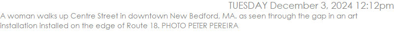 A woman walks up Centre Street in downtown New Bedford, MA. as seen through the gap in an art installation installed on the edge of Route 18. PHOTO PETER PEREIRA