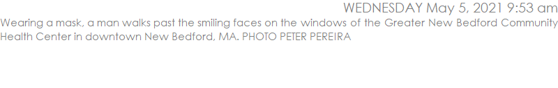 Wearing a mask, a man walks past the smiling faces on the windows of the Greater New Bedford Community Health Center in downtown New Bedford, MA. PHOTO PETER PEREIRA