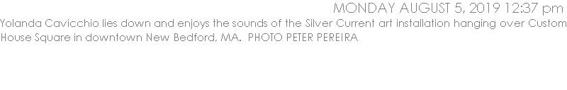 Yolanda Cavicchio lies down and enjoys the sounds of the Silver Current art installation hanging over Custom House Square in downtown New Bedford, MA.  PHOTO PETER PEREIRA