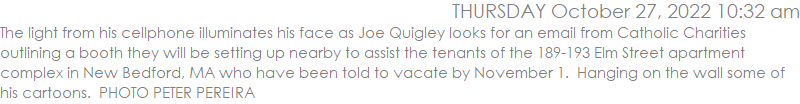The light from his cellphone illuminates his face as Joe Quigley looks for an email from Catholic Charities outlining a booth they will be setting up nearby to assist the tenants of the 189-193 Elm Street apartment complex in New Bedford, MA who have been told to vacate by November 1.  Hanging on the wall some of his cartoons.  PHOTO PETER PEREIRA