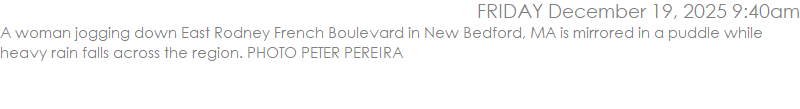 A woman jogging down East Rodney French Boulevard in New Bedford, MA is mirrored in a puddle while heavy rain falls across the region. PHOTO PETER PEREIRA