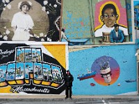 Security guard Jim Cabral is flanked by a set of colorful 'postcard' murals as he monitors parking at the Bank of America parking lot on Elm Street in downtown New Bedford.