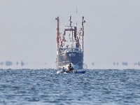 A man fishes from a kayak as a fishing boat seemingly heads towards him in the distance as see from Fort Phoenix in Fairhaven.