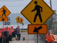 A woman and two dogs are surrounded by pedestrian crossing signs as they make their way down the Blue Lane walk along East Rodney French Boulevard, while another jogs.