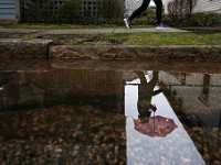 A woman is reflected on a puddle on the side of the road as she makes her way up Union Street in New Bedford on a rainy day.