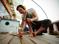 GarettEisele, of Clark & Eisele Traditional Boatbuilding, uses a mallet and a calking iron, to install new tarred hemp fiber into the gaps between the planks on the foredeck of the Ernestina-Morrissey schooner docked at State Pier in New Bedford.