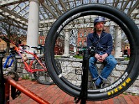 Adam Wells is seen through the wheel of one of his sons bike wheels while sits on the retaining wall while his kids are free to play at Custom House Square in New Bedford during a bike ride.