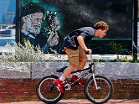 A young man rides his bicycle up MacArthur Drive in New Bedford past a painting of a sailor using a sextant.