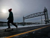 A man rides his skateboard along the Cape Cold canal in Buzzards Bay, in the background the iconic rail bridge.